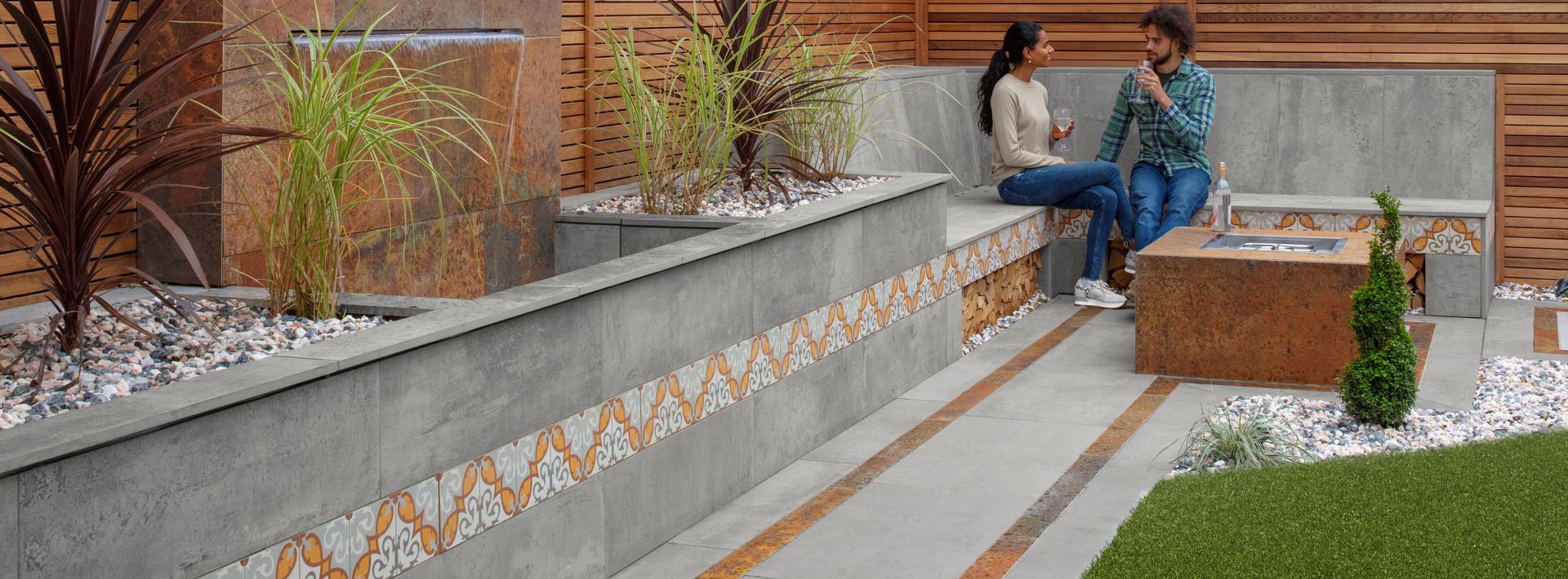 Marshalls Symphony metallic grey paving laid in a garden with two people sat on grey seating talking