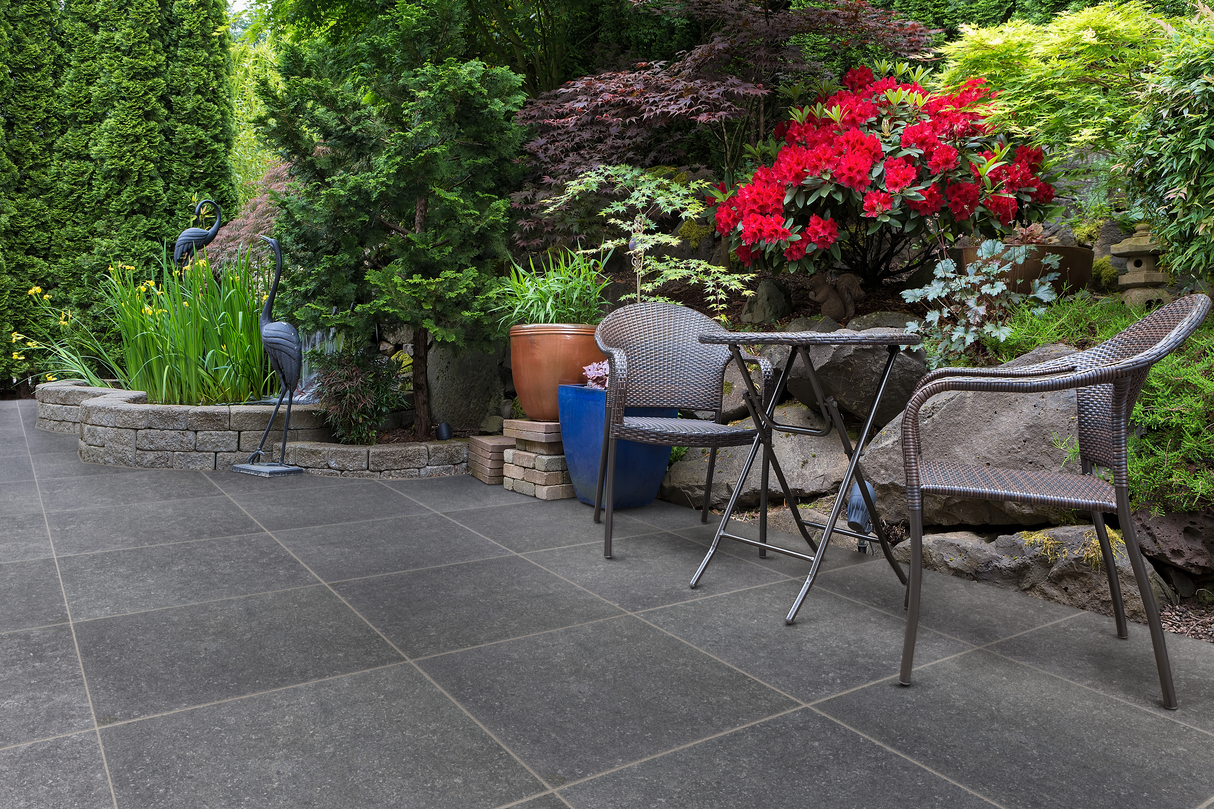 SYMPHONY® Plus Classic in Dark Grey A dark grey patio with a table and chairs and a backdrop of red flowers